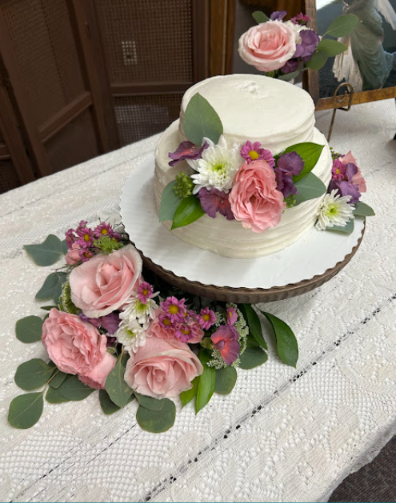 White wedding cake decorated with pink roses and purple flowers