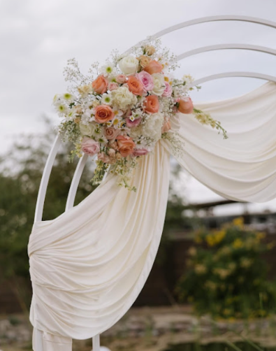 Cream-draped wedding arch with peach, blush, and ivory flowers